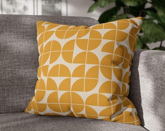 May include: Square cushion featuring a geometric design of yellow semi-circles and white lines on a cream backdrop. The cushion is placed on a grey sofa, creating a modern look. The cushion is approximately 45 cm square.