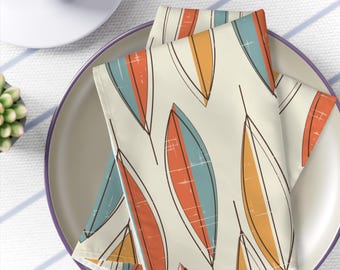 May include: Two folded fabric napkins with a geometric pattern of orange, blue, and yellow leaves on a white background.