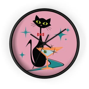 May include: A black cat with a red bow tie and a martini glass design on a round wall clock. The clock face is pink with teal starbursts and a black bezel. The clock hands are black.