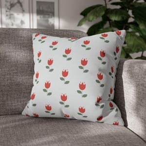 May include: A white throw pillow with a repeating pattern of red tulips with green stems on a white background.