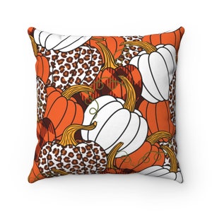 May include: Square throw pillow with a fall-themed pumpkin pattern. The design features orange, white, and leopard print pumpkins with brown stems and green vines. The background is white.