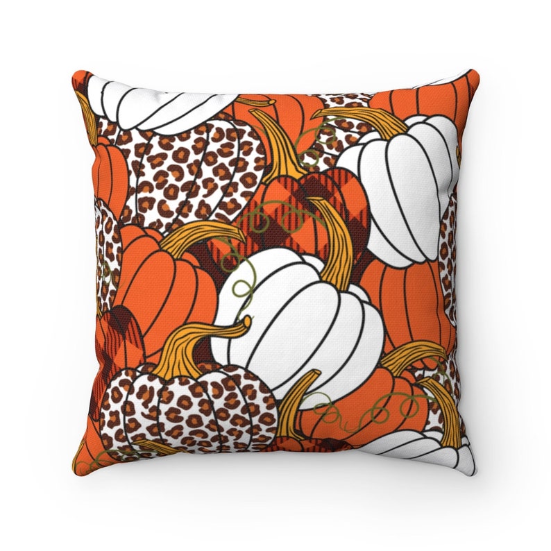 May include: Square throw pillow with a fall-themed pumpkin pattern. The design features orange, white, and leopard print pumpkins with brown stems and green vines. The background is white.