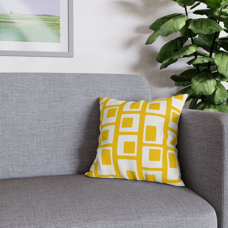 Pu&ograve; includere: Un cuscino per divano grigio con un motivo geometrico giallo e bianco.