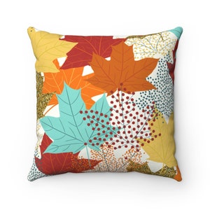 May include: Square throw pillow with a colorful autumn leaf pattern. The design features maple leaves in shades of orange, red, yellow, and teal, with accents of gold glitter and dotted patterns. The pillow is square-shaped.