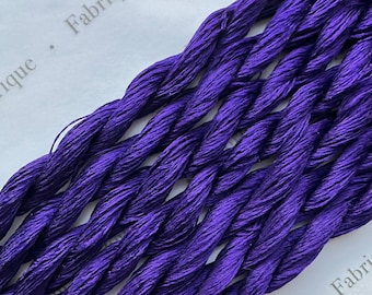 May include: A close-up of a bundle of purple embroidery floss. The floss is twisted and has a slight sheen. The text "Fabrique" is visible in the background.