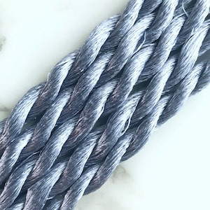 May include: Close-up of a bundle of silver-grey embroidery floss. The floss is twisted and has a subtle sheen.