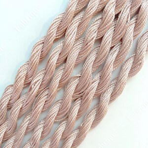 May include: A close-up of several strands of light pink embroidery floss, twisted together.