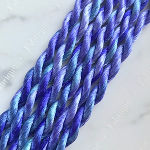 May include: A close-up of several strands of blue and purple embroidery floss. The floss is twisted and has a gradient of color from light blue to dark purple.