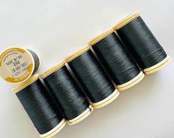 Op de afbeelding: Een aantal spoelen zwart naaigaren, diagonaal gerangschikt. De spoelen hebben lichtbruine uiteinden, en één spoel toont een label met de tekst "SOIE N°30 494".