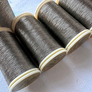 May include: Five spools of metallic thread in a silver and black color. The thread is wound around white plastic spools with black text.