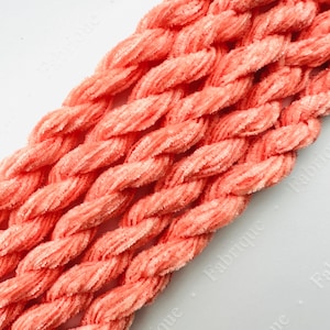 May include: A close-up of a bundle of coral-colored chenille stems. The stems are twisted together and have a soft, fuzzy texture.