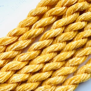 May include: Close-up of a bundle of yellow chenille stems, also known as pipe cleaners. The stems are twisted together and have a soft, fuzzy texture.