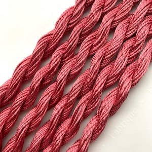 May include: Close-up of a bundle of six strands of deep red embroidery floss.