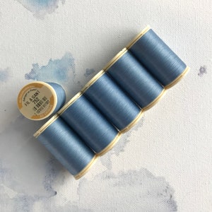 May include: Six spools of light blue thread, arranged in a row, with one spool lying separately. The label on the spool reads "Fil A Gant 752".