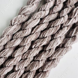 May include: Close-up of a bundle of soft, light brown velvet yarn. The yarn is twisted and has a fuzzy texture.