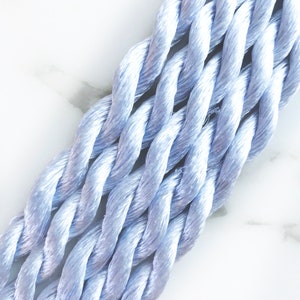 May include: A close-up of a bundle of light blue embroidery floss. The floss is twisted together in a rope-like shape.