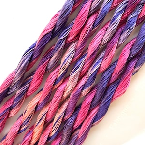 May include: A bundle of six strands of twisted embroidery floss in shades of pink, purple, and peach.