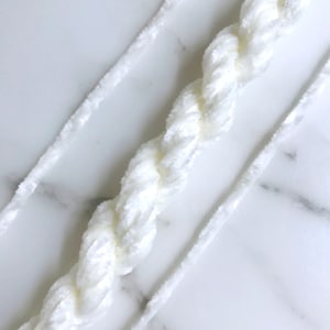Op de afbeelding: Drie witte strengen garen, twee zijn dun en één is dik en pluizig.
