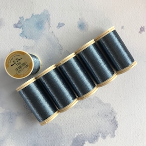 May include: Six spools of metallic blue thread, each with a beige label. The label on one spool reads "N°40 METAL 100 AU CHINOIS".