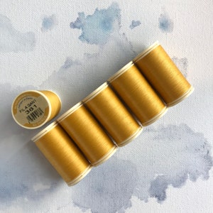 May include: Six spools of gold thread, each with a white label. The label on one spool reads "Fil A Gant 36/1 Au Crochet".