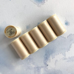 May include: Six spools of beige thread, arranged in a semi-circle, with a single spool of beige thread labeled "FIL A GANT 308" in the upper left corner.