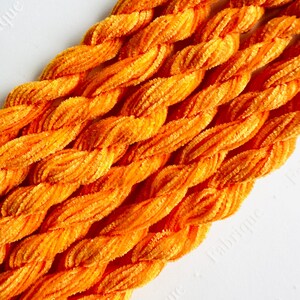 May include: Close-up of a bundle of orange chenille stems, also known as pipe cleaners, in a braided pattern. The stems are soft and fluffy, and they are perfect for crafting.
