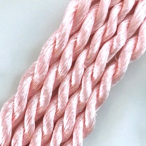 May include: Close-up of a bundle of soft, pink embroidery floss. The floss is twisted and has a subtle sheen.