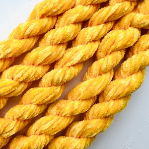 May include: Close-up of a length of yellow, braided rope. The rope has a soft, textured appearance and is made up of multiple strands twisted together. The color is a bright, sunny yellow, with subtle variations in tone.