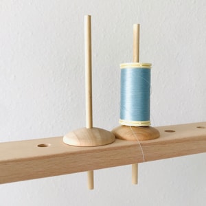 May include: A wooden thread holder with two spools. One spool is empty and the other is filled with light blue thread.
