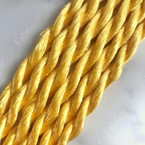 May include: Close-up of a bundle of bright yellow embroidery floss. The floss is twisted together in a rope-like shape.