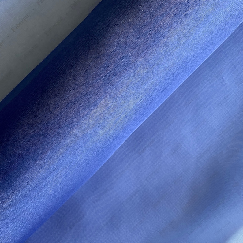 May include: A roll of sheer blue fabric with a subtle sheen. The fabric is lightweight and translucent, making it ideal for crafting and sewing projects.