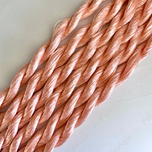 May include: A close-up of several strands of peach-coloured embroidery floss. The floss is twisted and has a soft, silky texture.