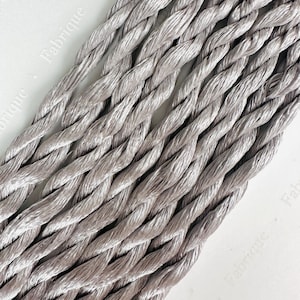 May include: Close-up of a bundle of silver-grey twisted embroidery floss. The floss is arranged in a criss-cross pattern, highlighting the texture and sheen of the thread.