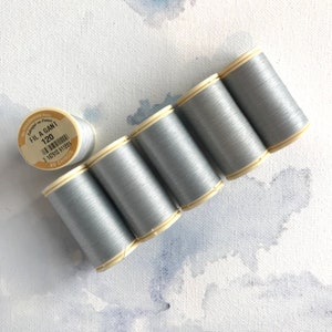 May include: Six spools of silver gray thread, each with a white label. The label on one spool reads "Fila Gant 120" and has a barcode.