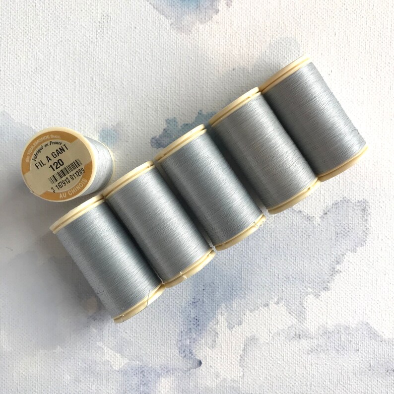May include: Six spools of silver gray thread, each with a white label. The label on one spool reads "Fila Gant 120" and has a barcode.
