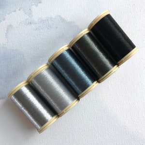 May include: Five spools of metallic thread in shades of silver, gray, blue, charcoal, and black.