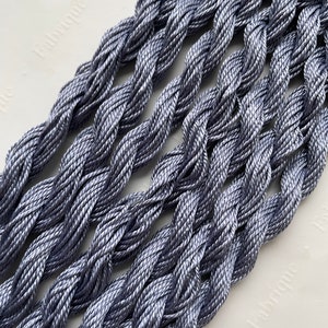 May include: Close-up of several strands of silver gray embroidery floss, twisted together in a woven pattern.