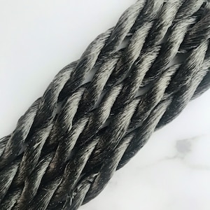 May include: Close-up of a black and white braided rope. The rope is made of multiple strands of yarn that are twisted together to create a thick, durable cord.