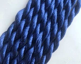 May include: A close-up of a bundle of dark blue embroidery floss. The floss is twisted and piled on top of itself, creating a textured look.