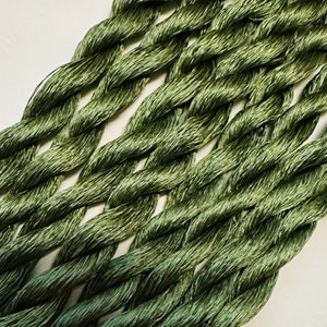 May include: A close-up of multiple strands of green embroidery floss, twisted together. The floss is a muted, dark green color.