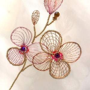 May include: A delicate gold and pink floral embroidery with purple and red rhinestones. The embroidery is on a white fabric background.
