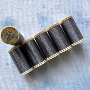 Puede incluir: Seis carretes de hilo metálico gris, cada uno con una bobina de plástico blanco. La etiqueta de un carrete dice "N°40 METAL 125 AU CHINOIS".