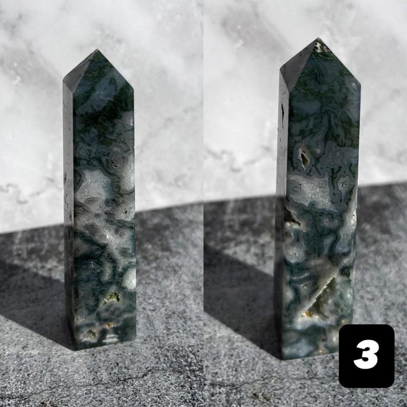 May include: Two polished moss agate obelisks. The obelisks are rectangular with a pointed top. The stone has a mix of white, green, and gray colors. The obelisks are standing on a gray surface. A black square with the number 3 is in the bottom right corner.