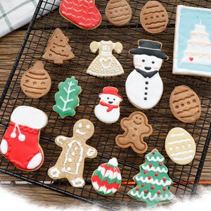 May include: A variety of Christmas-themed cookies decorated with colorful icing. The cookies are arranged on a wire rack and include shapes such as a stocking, a snowman, a gingerbread man, a Christmas tree, and a candy cane.