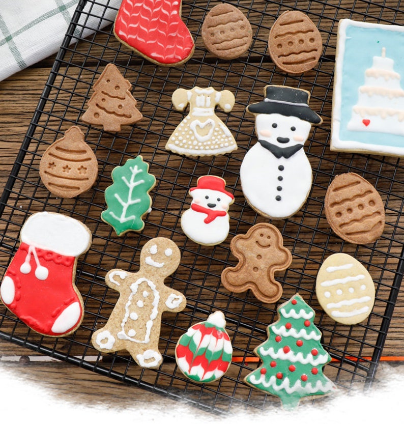 May include: A variety of Christmas-themed cookies decorated with colorful icing. The cookies are arranged on a wire rack and include shapes such as a stocking, a snowman, a gingerbread man, a Christmas tree, and a candy cane.