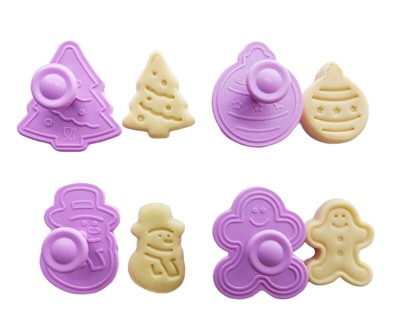 May include: Set of eight purple plastic cookie cutters in the shapes of a Christmas tree, a snowman, a gingerbread man, and a Christmas ornament. The cutters are paired with matching cookies.