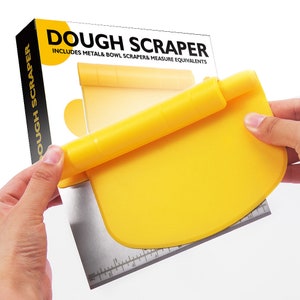 Puede incluir: Raspador de masa amarillo con una regla de metal en la parte inferior. El raspador está enrollado y se sostiene en una mano. El embalaje dice "Dough Scraper" e "Includes Metal & Bowl Scraper & Measure Equivalents".