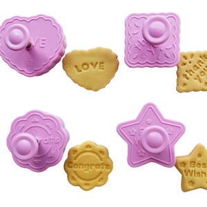 May include: Set of six pink plastic cookie cutters with different shapes and designs. The cutters are used to create cookies with the words "Love", "Congrats", "Best Wishes", "Thank You", "Congrats" and "Star".
