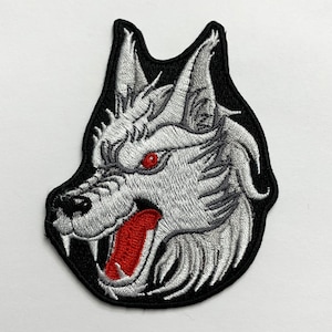 May include: Iron-on patch featuring an embroidered white wolf's head with red eyes and an open mouth, set against a black background.
