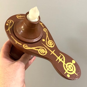 May include: A brown ceramic lamp with a white top and gold painted swirls and designs. The lamp is shaped like a genie lamp.